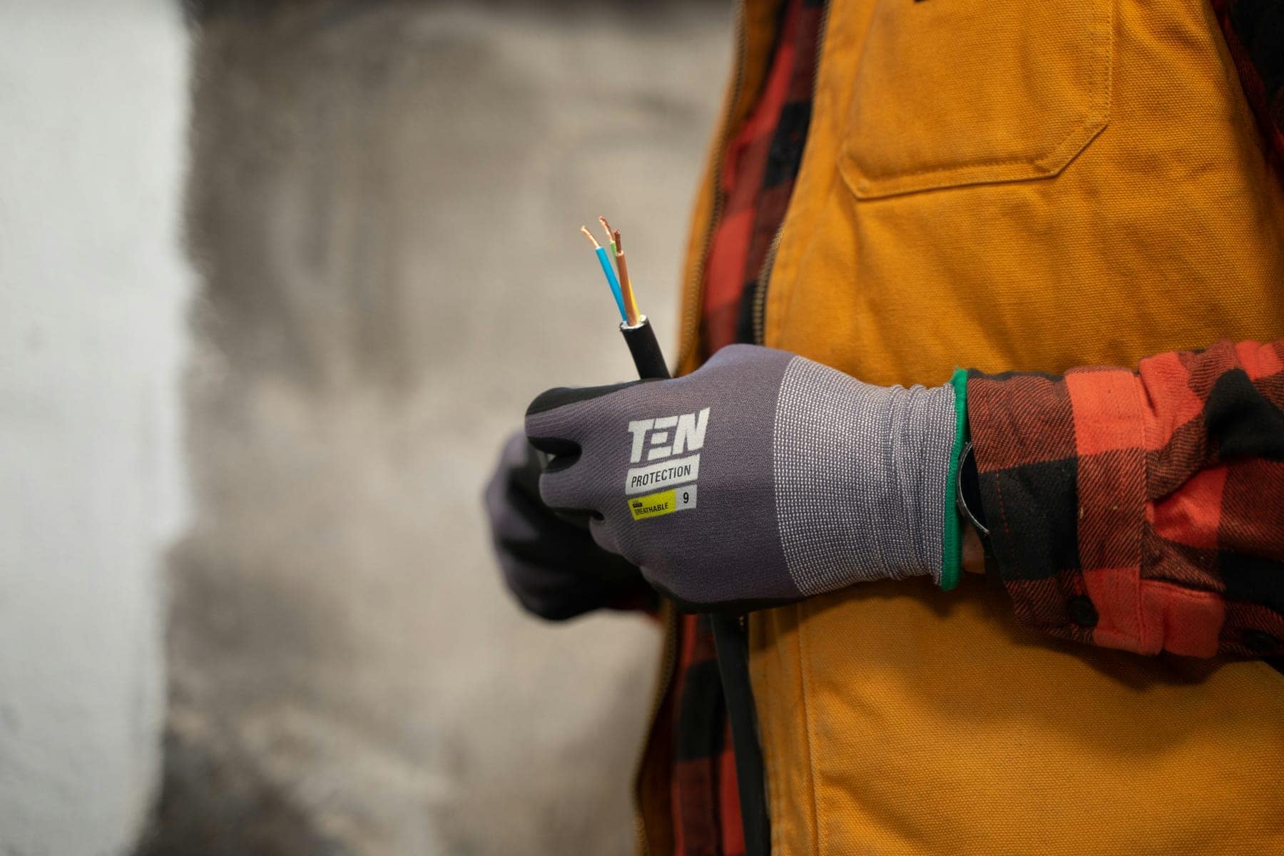 Hand im Arbeitshandschuh hält ein abisoliertes Kabel